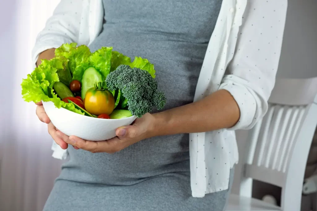 Pregnant woman with bowl of fresh vegetables, broccoli, leaf salad, tomato.